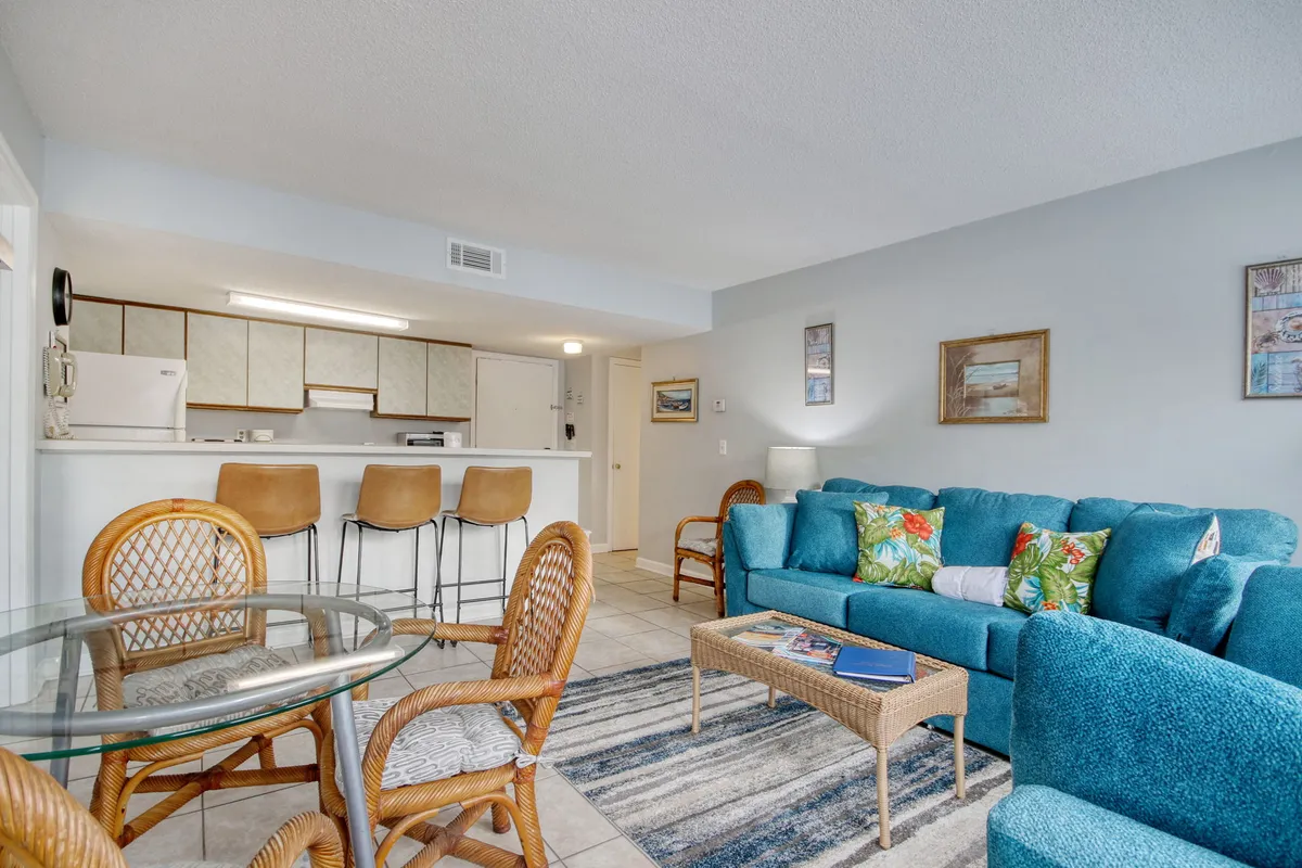 A bright and inviting living-dining area with a turquoise sofa, glass dining table, and bar stools. The arrangement encourages both socializing and shared meals, providing a glimpse into spaces where stories and laughter flow naturally.