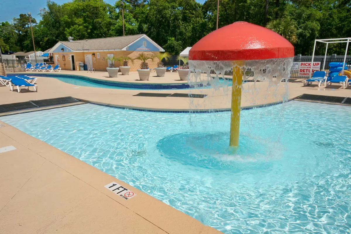 A cheerful exterior shot of a pool area featuring a vibrant, colorful water feature, a spacious swimming pool, and plenty of sun loungers. The area is designed for fun, relaxation, and family-friendly enjoyment under the sun.