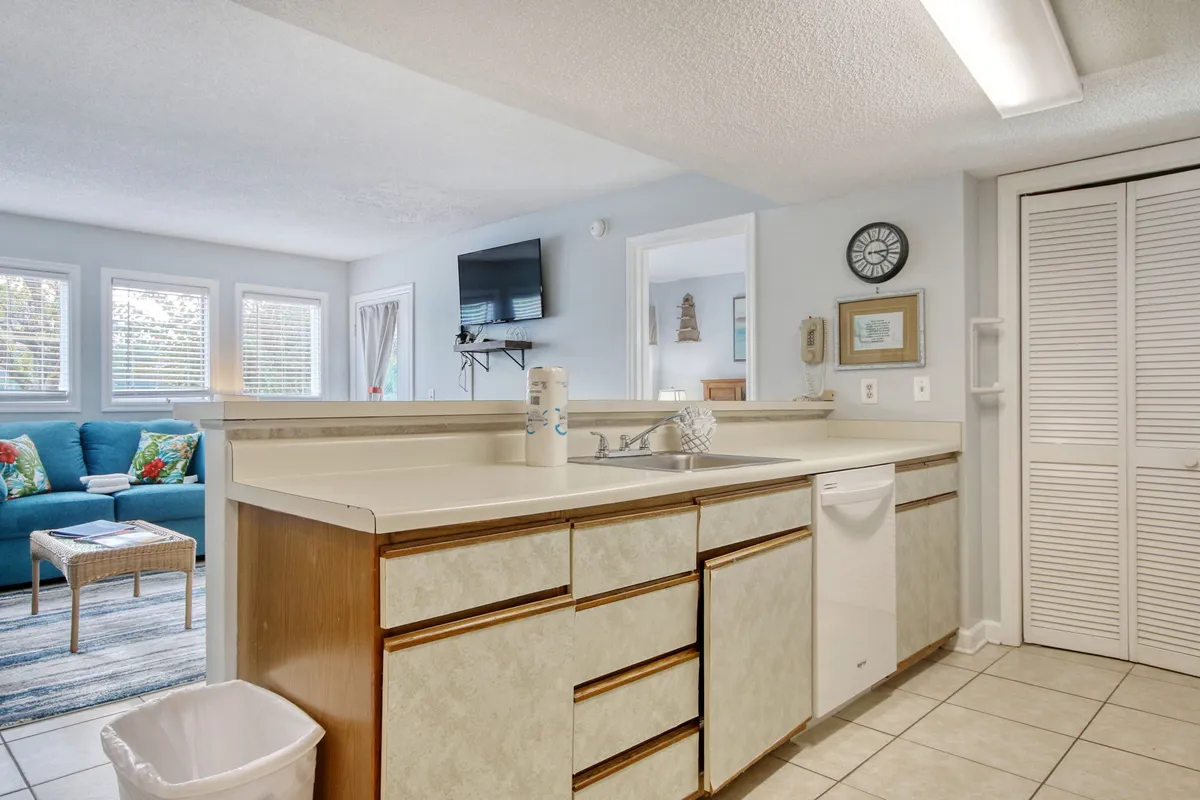 An inviting open-plan space featuring a kitchen counter with a visible sink and dishwasher, seamlessly flowing into a living area with a cozy blue couch. The scene is set for both meal preparation and comfortable entertaining, with ample space for family gatherings and celebrations.