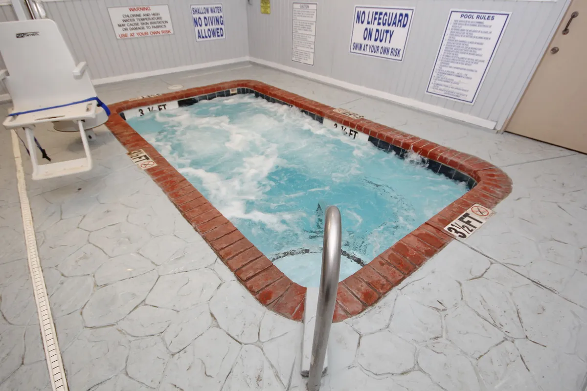 An inviting indoor hot tub area with seating around the bubbling spa, signage for pool rules, and a relaxed atmosphere for guests to unwind after a day of water fun.